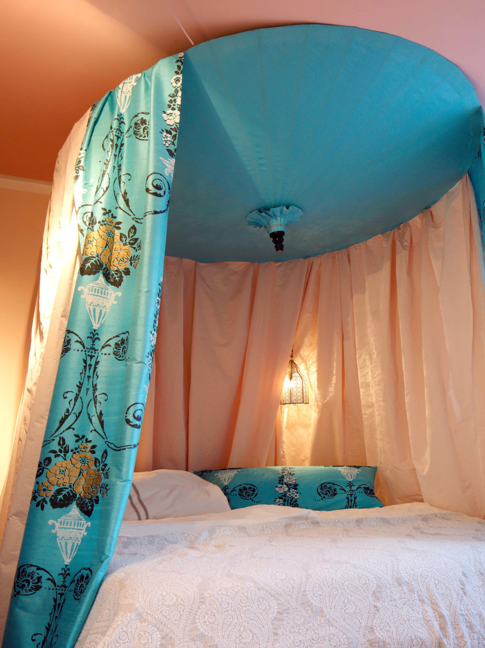 Bett mit hängendem Baldachin aus zwei verschiedenen Stoffen in Hellblau mit goldenen Blüten und Pastellorange.