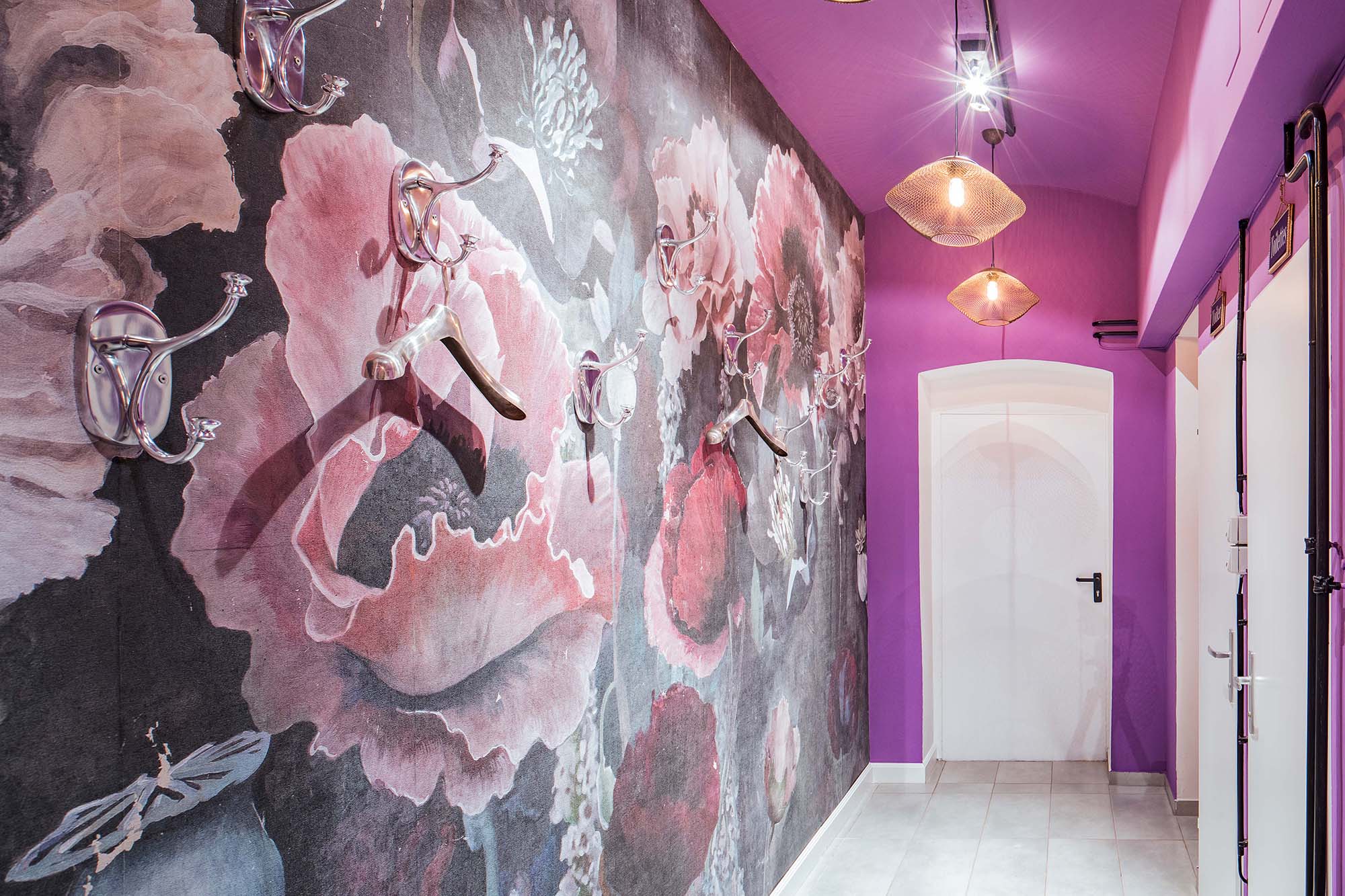 Zu Garderobe umgearbeiteter Flur, dank großer Chrom-Wandhaken mit Kleiderbügeln, montiert an tapezierter Wand mit großen Mohnblumen.