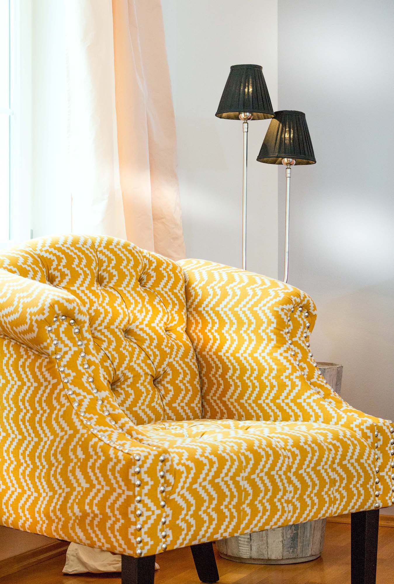 Gelb-weiß gemusterter Sessel mit Designlampe.