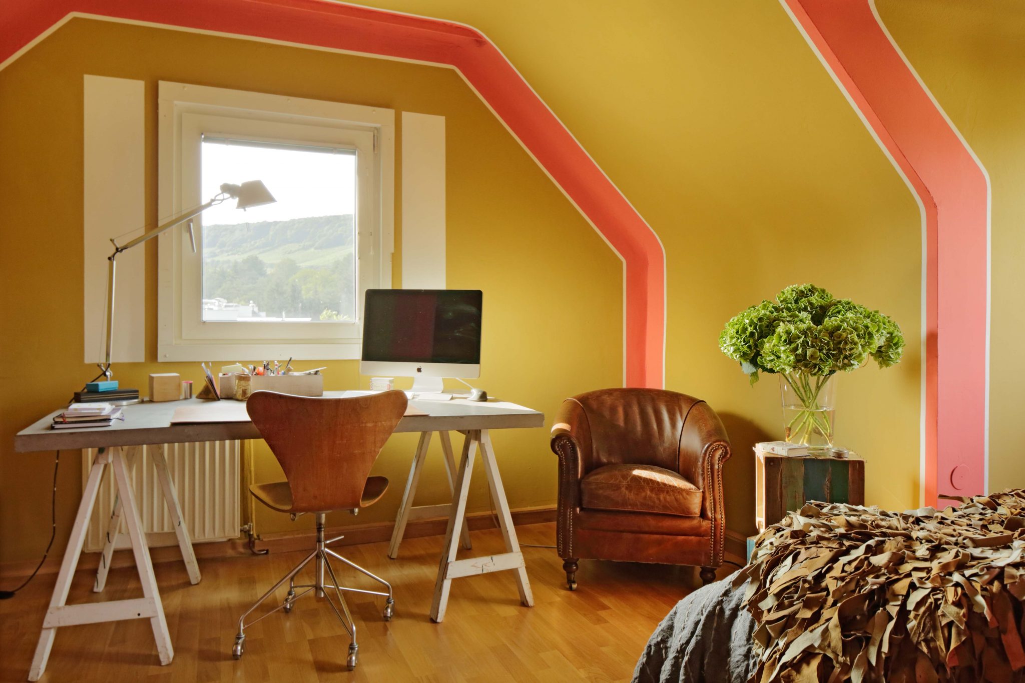 Durch Farbgestaltung in Bananengelb und Orange hervorgehobe Dachschrägen mit schlicht-elegantem Interior, Ledersessel, Schreibtisch und Bett.