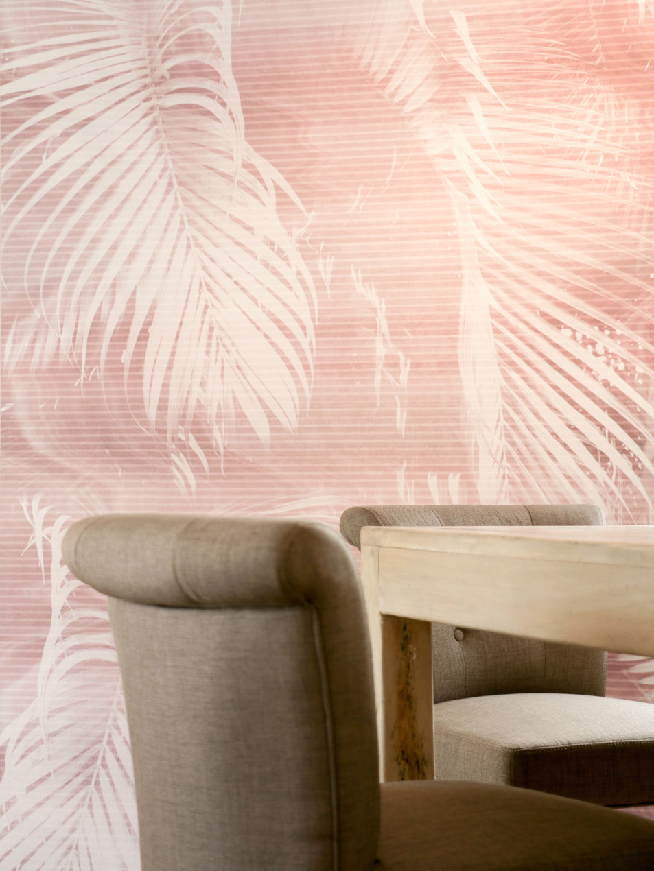 Esstisch in hellem Holz mit hellbraunen Stühlen vor Wand mit Tapete in Altrosa mit weißen Palmenblättern.