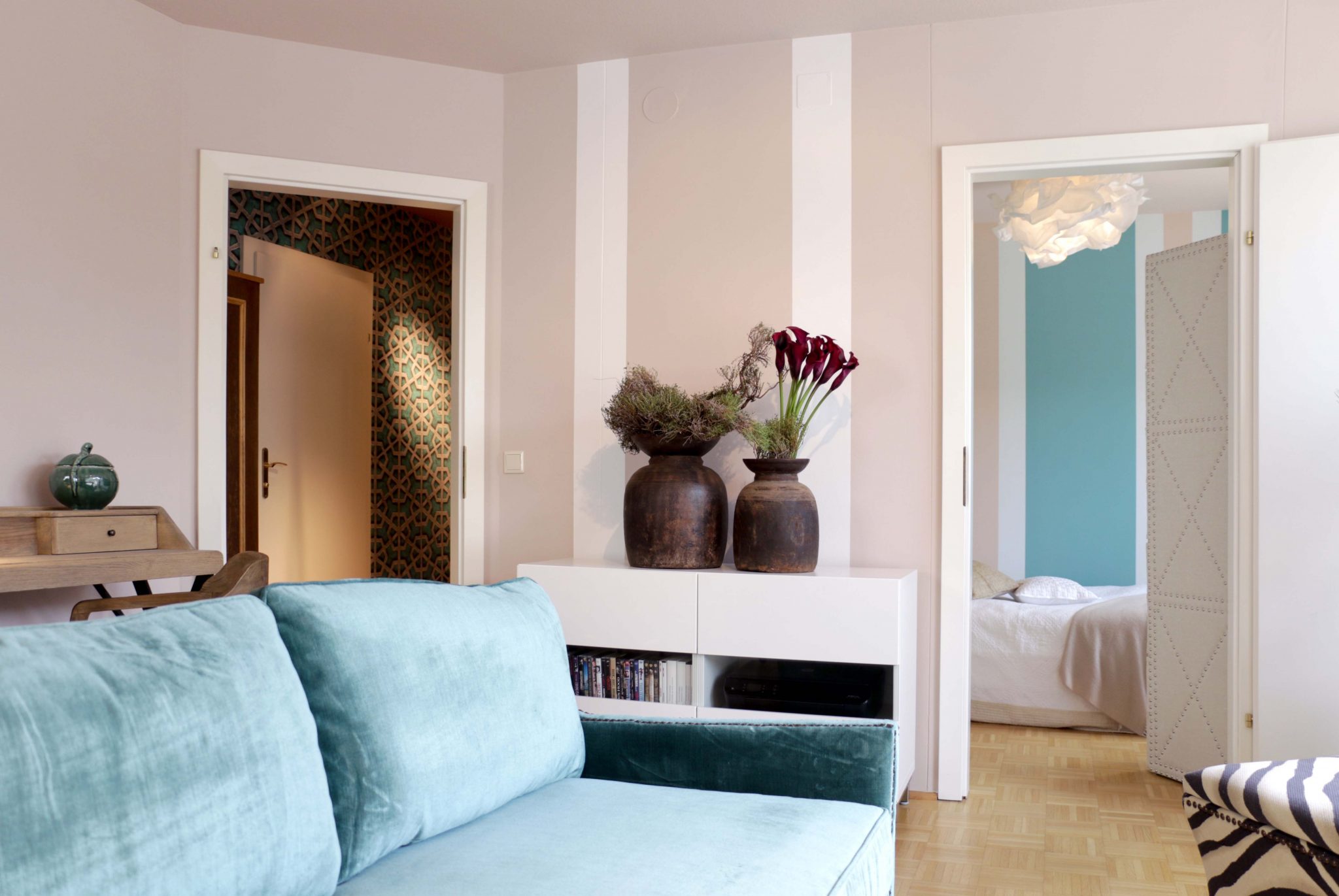 Beige und Weiß abgesetzte Wände mit azurblauem Samtsofa, Blick ins angrenzende Schlafzimmer mit beiger und türkiser Wandfarbe.
