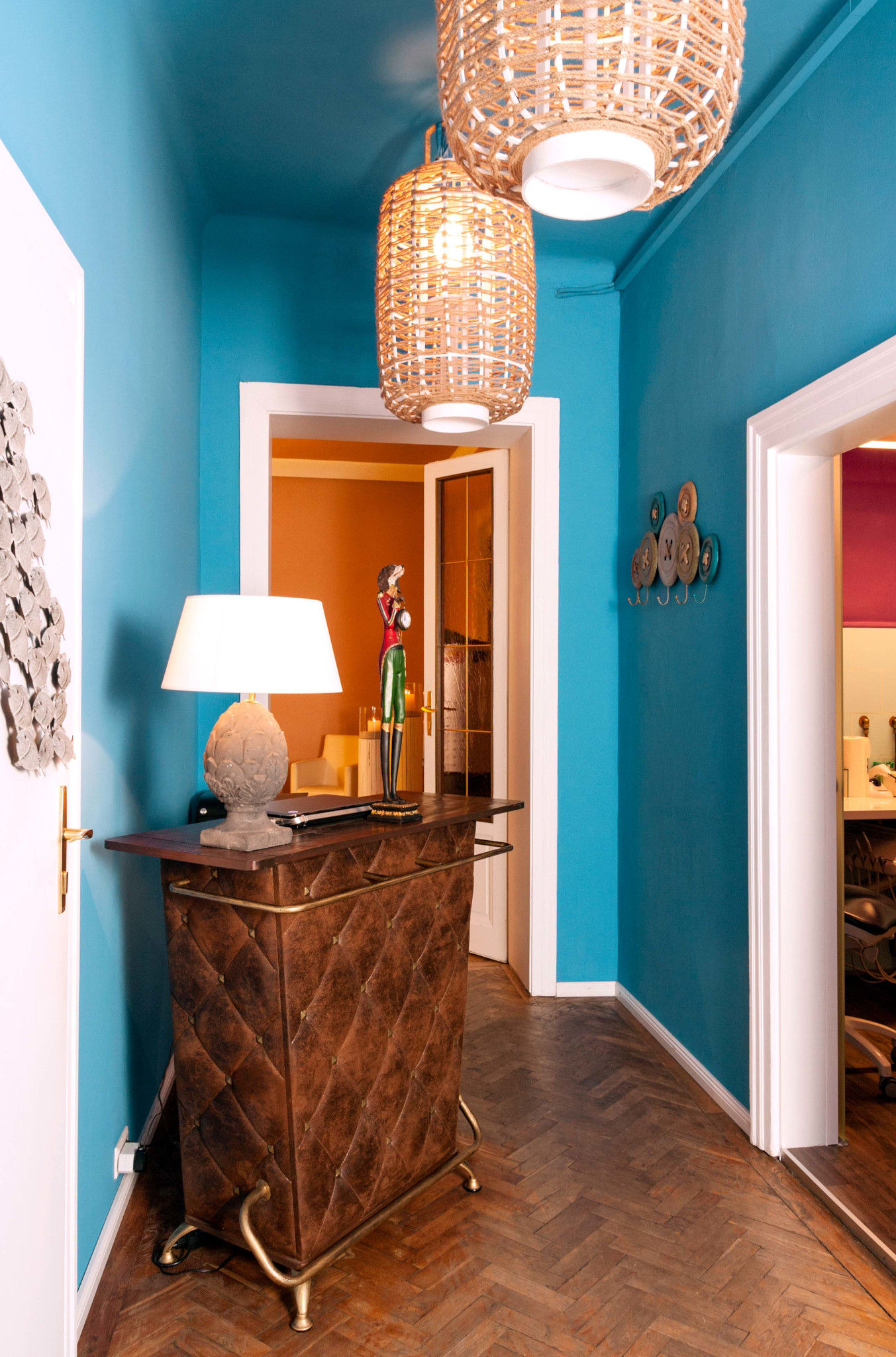Eingerichtet mit lederbezogenem Empfangstresen, blauer Wandfarbe, Parkettboden, Garderobenhaken und ovalen Lampen mit dickem Garn als Schirm.
