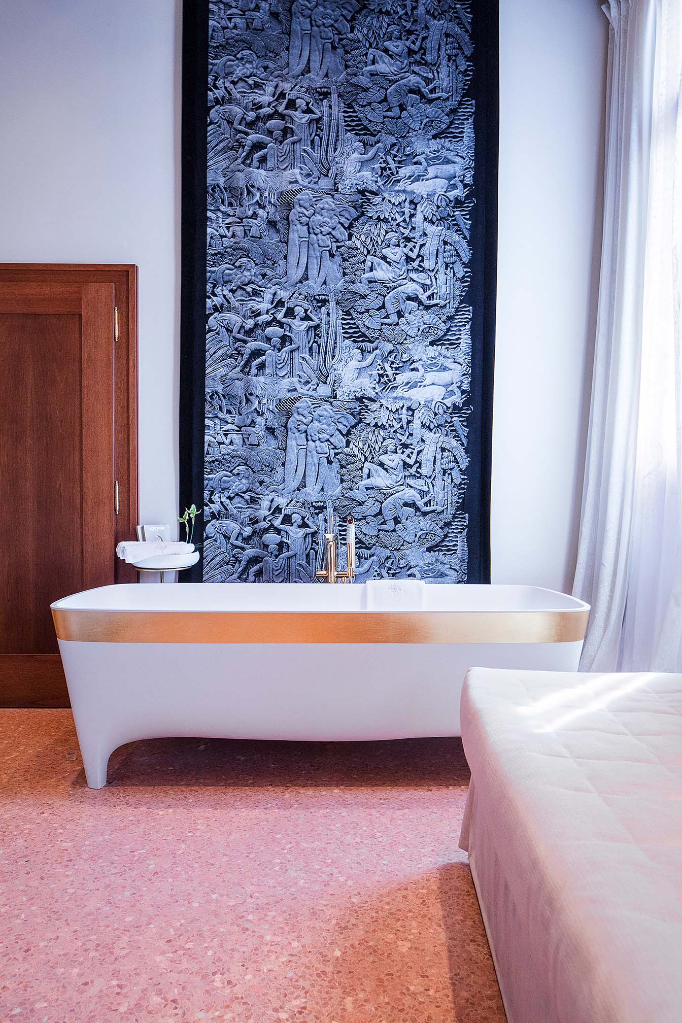 Freistehende Badewanne mit Goldrand vor schwarz-grauem Wandbehang mit Reliefmotiv