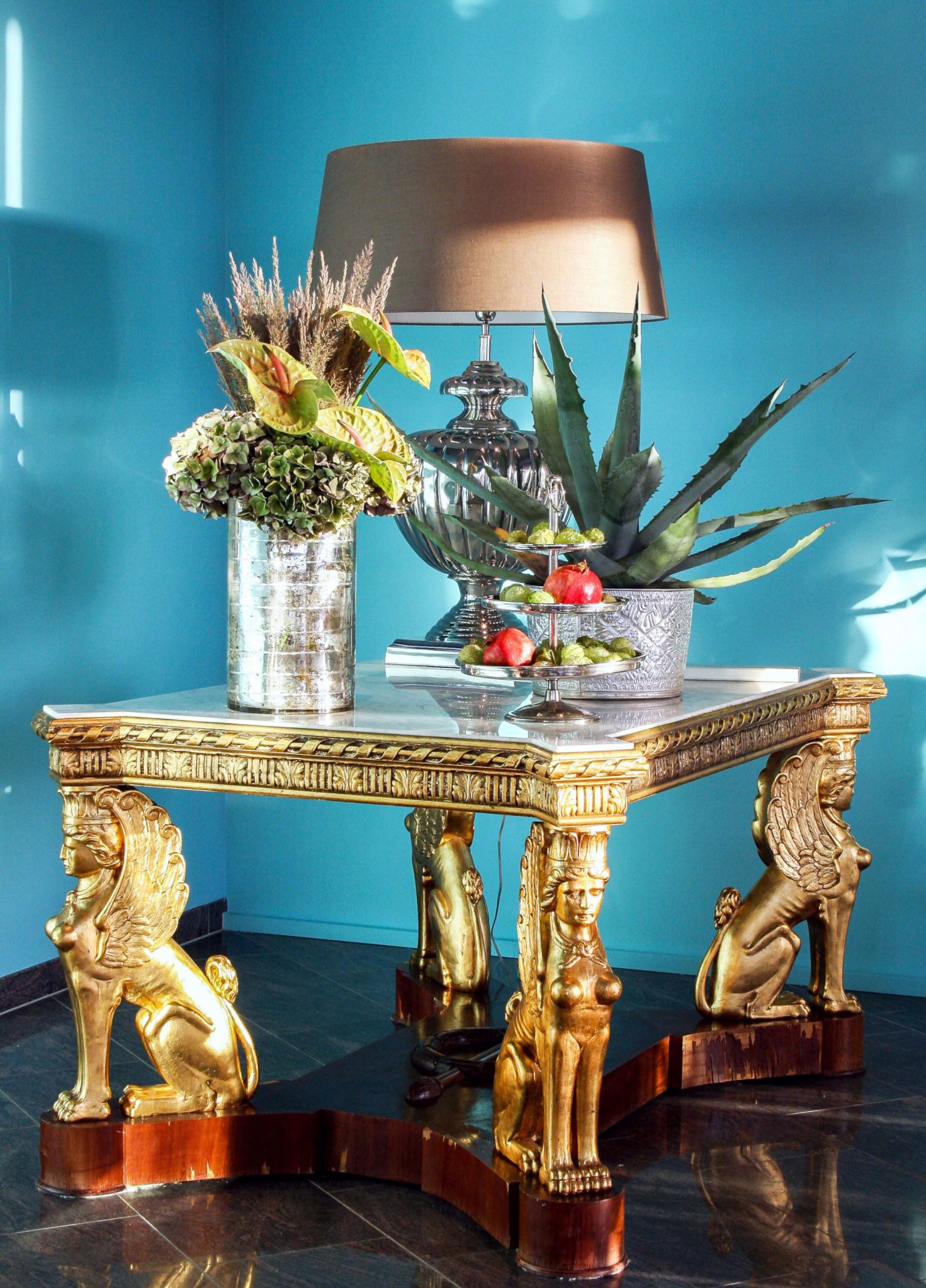 Antiker Sphinxtisch mit Goldverzierung und Marmorplatte. Lampe, Blumen und Etagere als Tischdekoration.