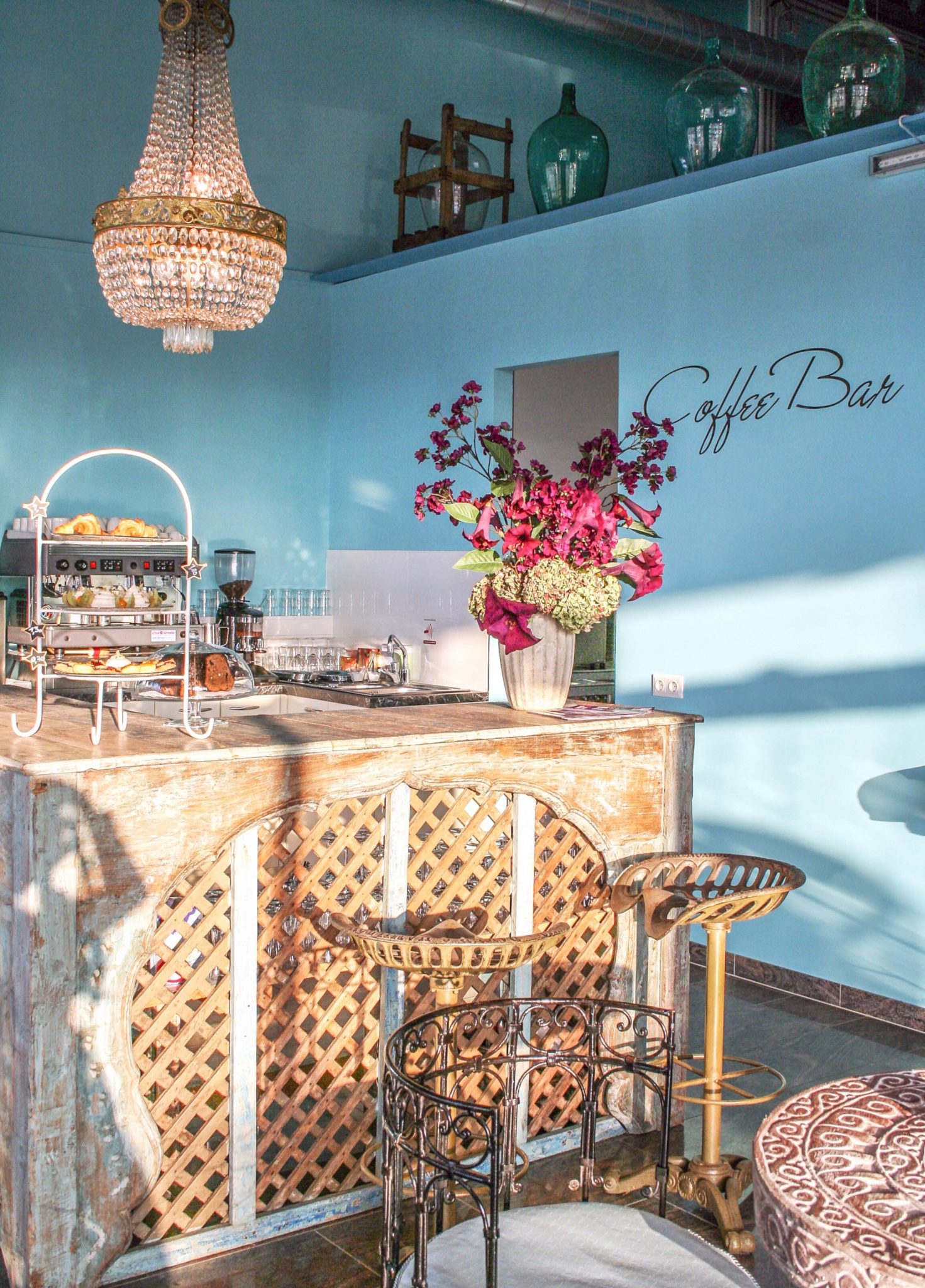 Freistehende Bar aus Holz mit weißer Etagere und Gefäß mit violetten Blumen als Dekoration vor blauer Wand.