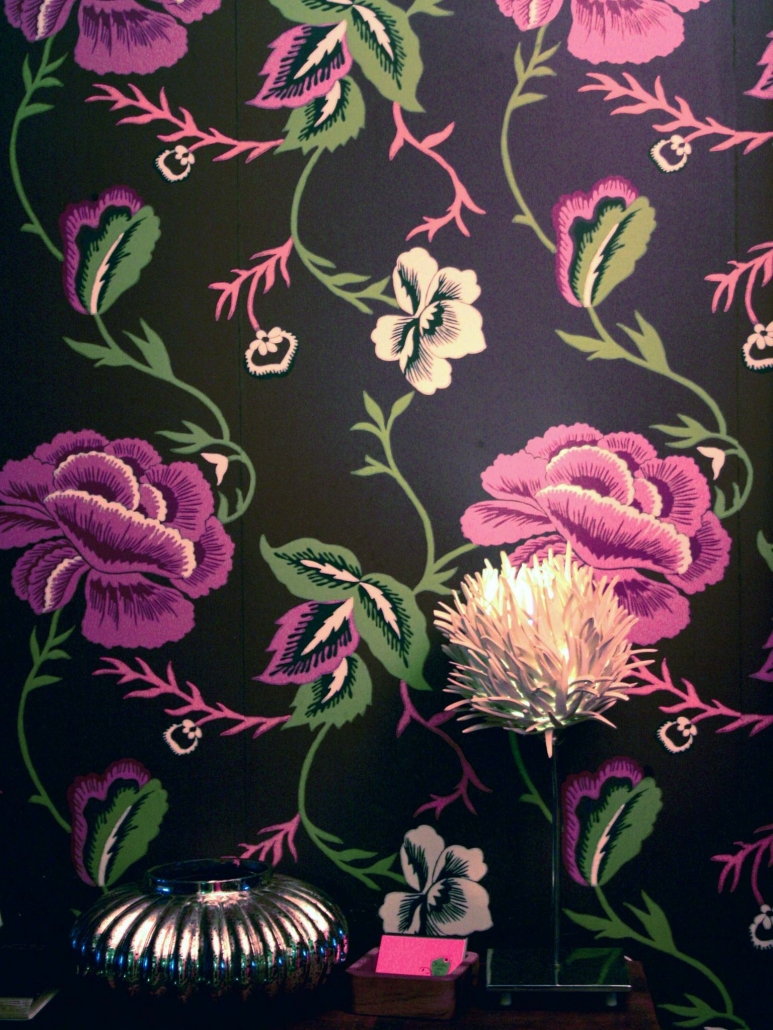 Sideboard mit Lampe und Blumenform und Tapete mit violetten Blumen.