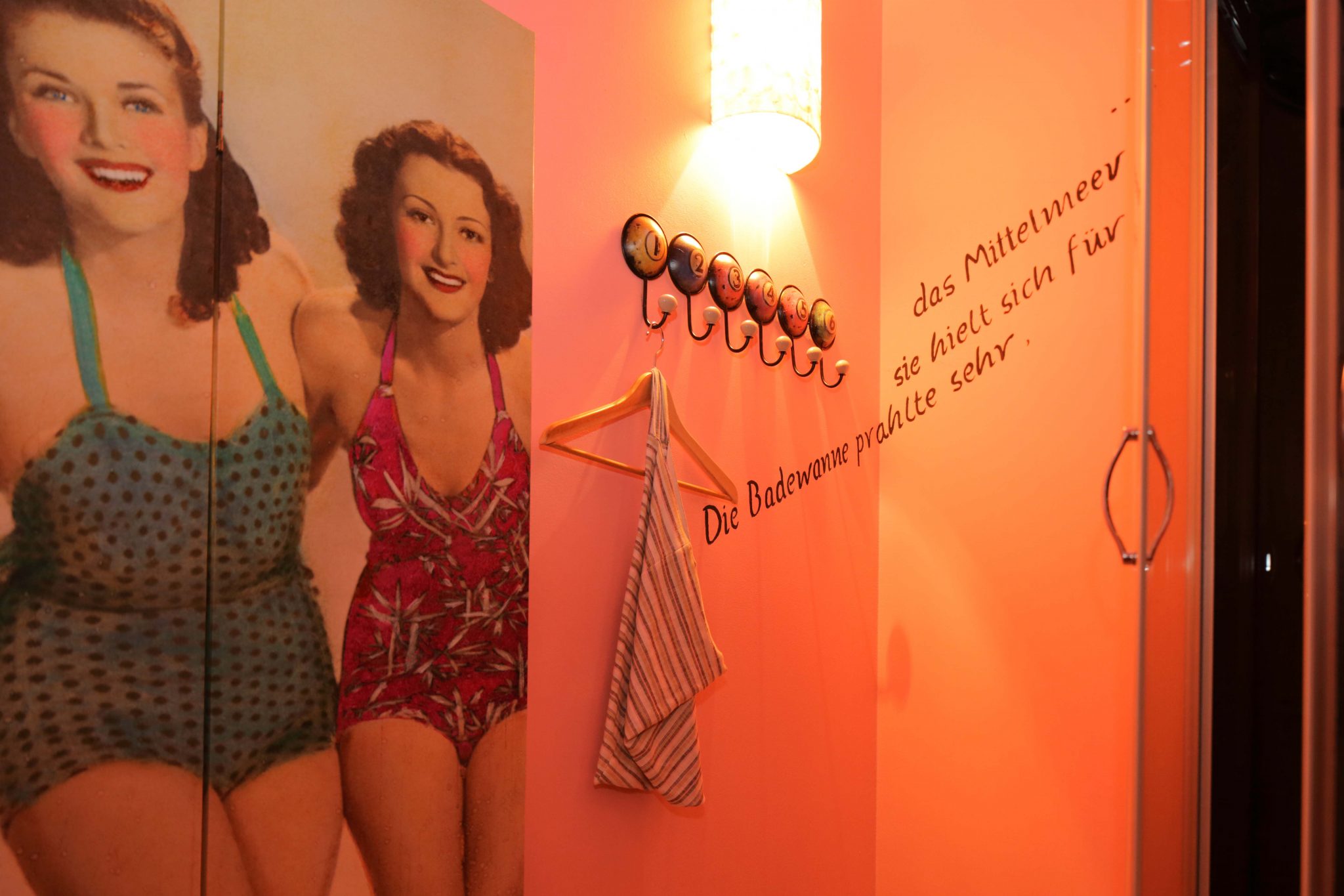 Paravent mit Frauenmotiv, runde Garderobenhaken in Billardkugel-Design und in Schwarz geschriebenes Zitat auf der Wand