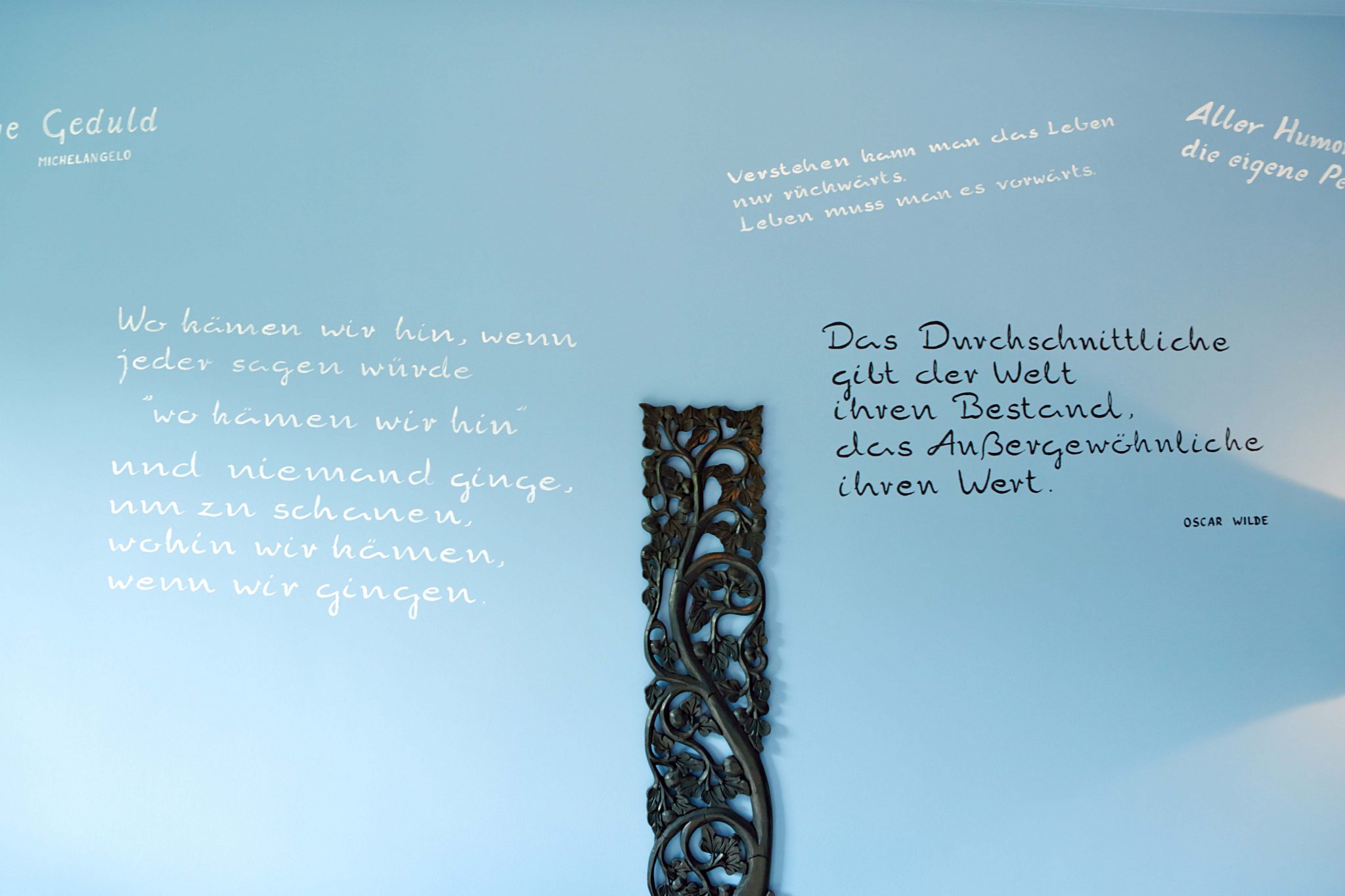 Blau gestrichene, mit Zitaten beschriebene Wand und floraler, schwarzer Wanddekoration aus Holz.
