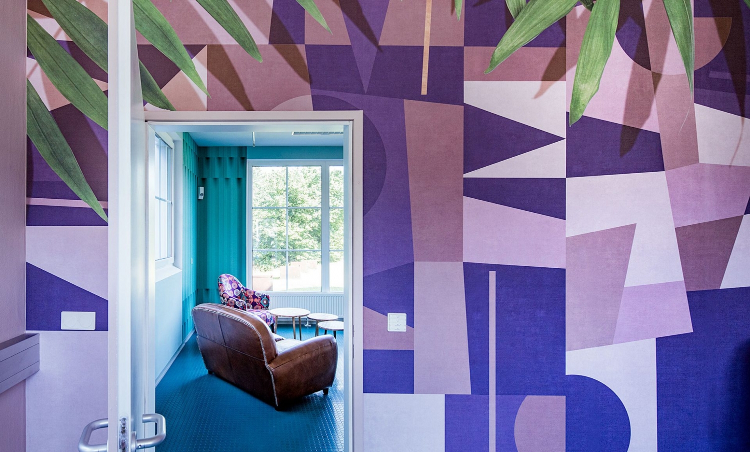 Grafisch gemusterte Tapete von Glamora in Violett-Tönen mit Palmenblätter in 3D-Effekt, passend zu türkisem Boden und Ledersofa