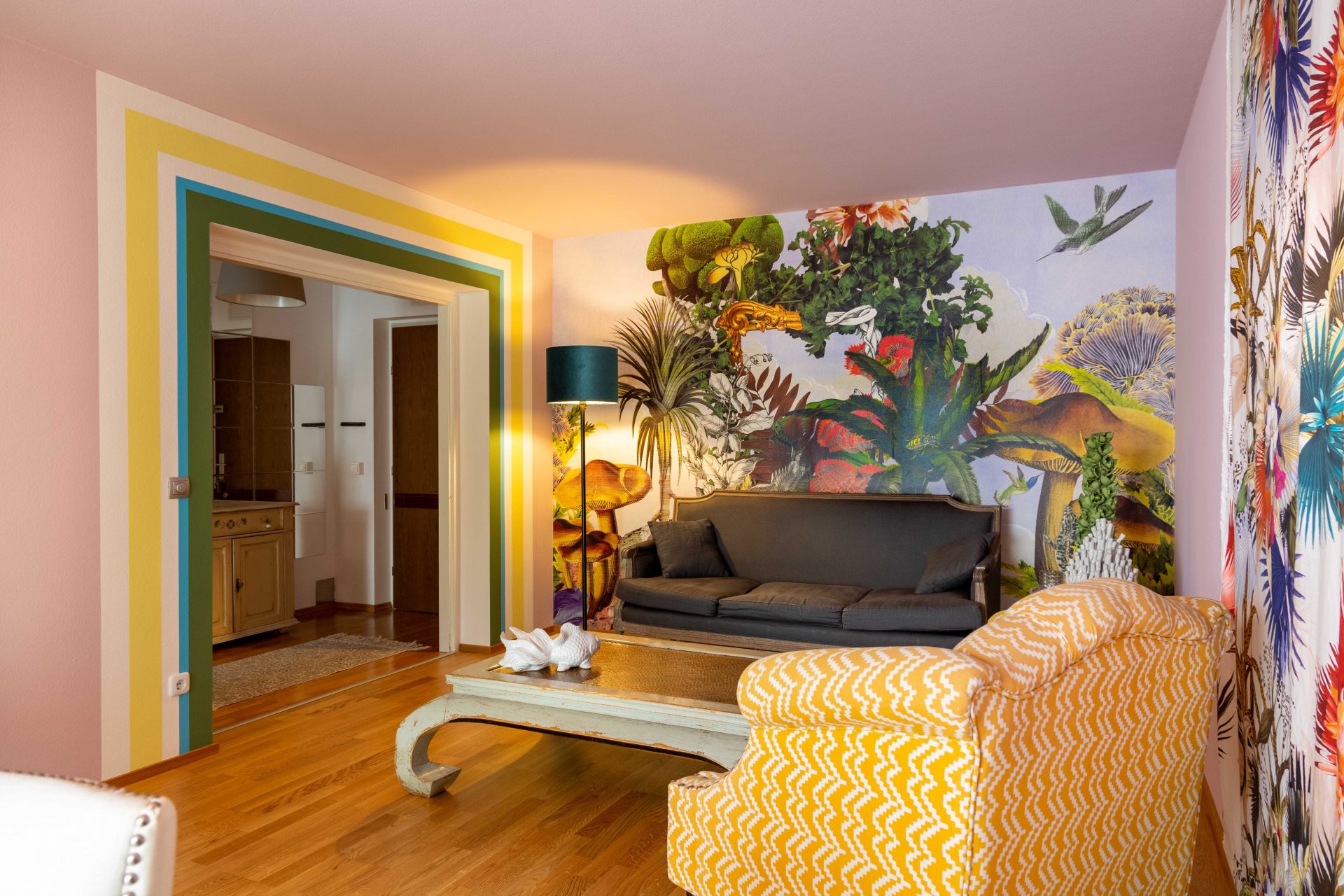 Wohnzimmer mit Lacroix-Tapete mit Pflanzen und Tieren und Lacroix-Stoffbahnen in Kombination mit verschiedenen Wandfarben und passenden Möbeln.