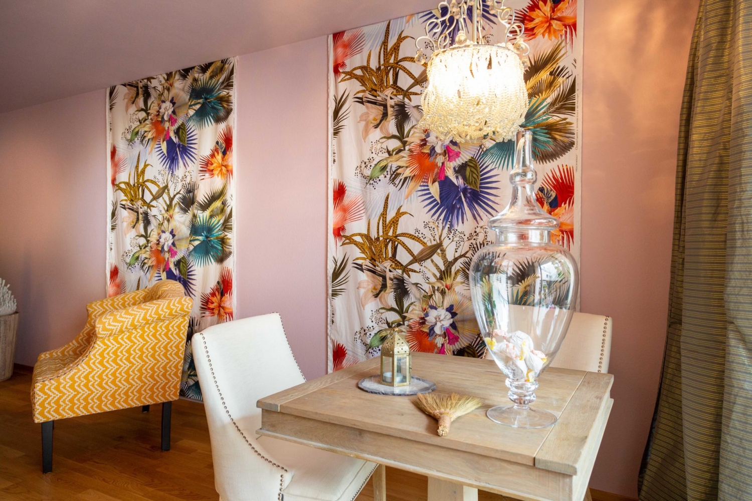 Kleiner Holztisch vor Lacroix-Wandbehang von Designers Guild mit verschiedenen blühenden Blumen und Pflanzen.