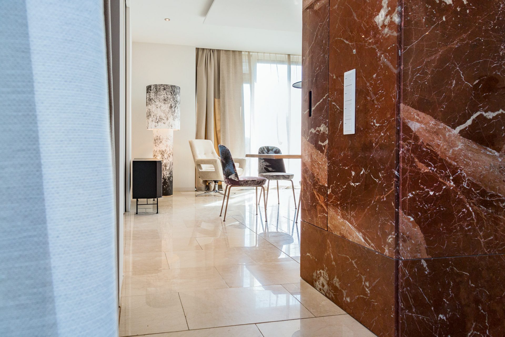 Blick von Küche ins Esszimmer mit hellem Marmorboden, großer Lodes Bodenleuchte und metallenem Sideboard.